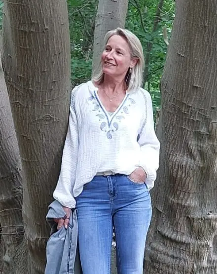 Edith staat lachend tussen de bomen in het bos