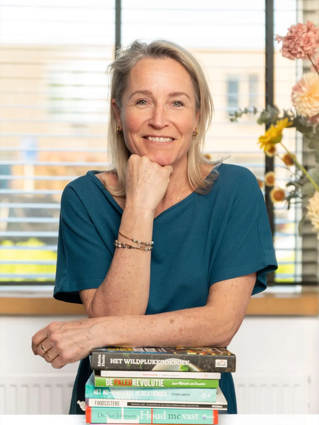 Edith Ruijs met haar kin op haar hand, leunend op een stapel boeken
