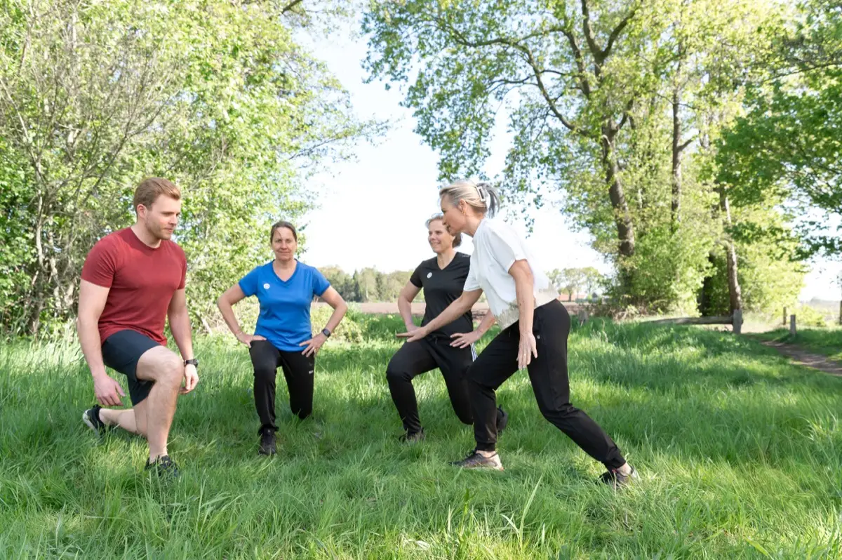 Edith doet buiten op het gras een uitvalspas voor, drie mensen doen mee